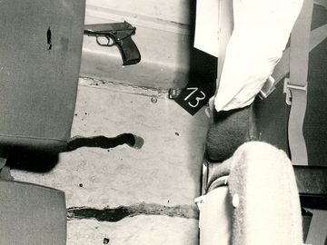 Zwei Pistolen liegen zwischen Sitzreihen auf dem Boden. In der Mitte des Bildes ist eine Blutspur zu sehen.