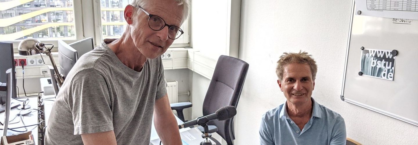 Maximilian Schönherr und Roger Engelmann sitzen in einem Büroraum und nehmen den Podcast auf.