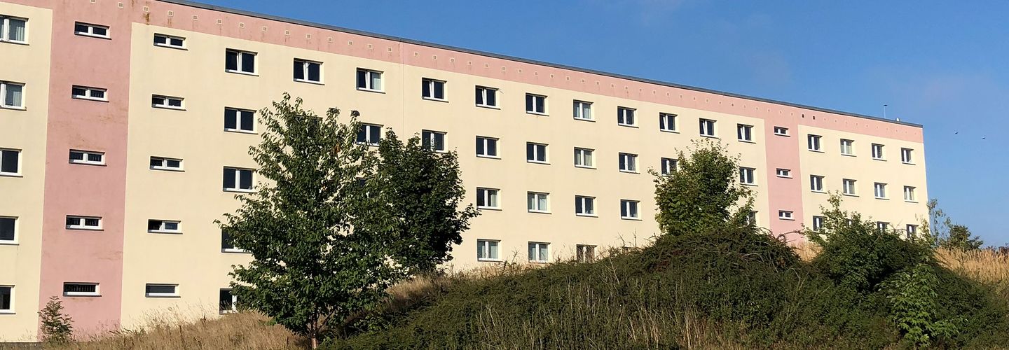 Das bild zeigt das Gebäude des Stasi-Unterlagen-Archivs in Rostock. Es handelt sich dabei um einen überwiegend gelben Plattenbau.