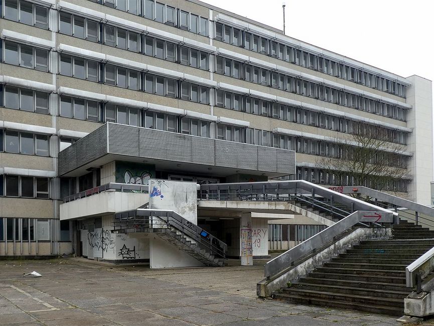 Das Bild zeigt den Eingang des ehemaligen Stasi-Krankenhauses in Berlin-Buch. Zum Eingang in der ersten Etage führt ein breite Treppe hinauf. Gebäude, Treppe und Vorplatz wirken heruntergekommen.