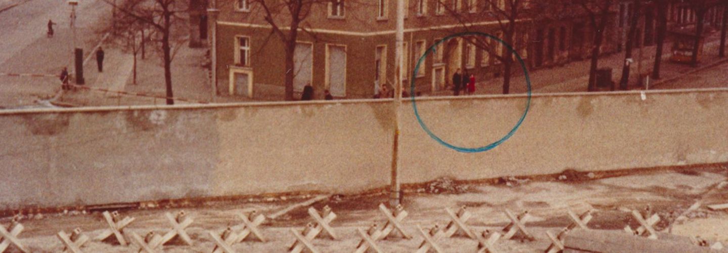 Blick von einer Besucherplattform in der Bernauer Straße auf Ost-Berlin. Vor einem Häuserblock steht eine kleine Gruppe von Menschen, die auf dem Foto in einem grünen Kreis markiert sind.