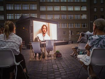 In der Dunkelheit schauen Menschen auf dem Innenhof der ehemaligen Stasi-Zentrale sitzend auf eine Kinoleinwand.