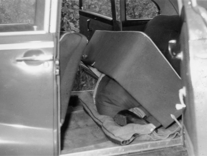 Zu sehen ist eine Person, die sich zusammengerollt unter einem hohlen Sitz in der Rückbank eines Pkw versteckt.