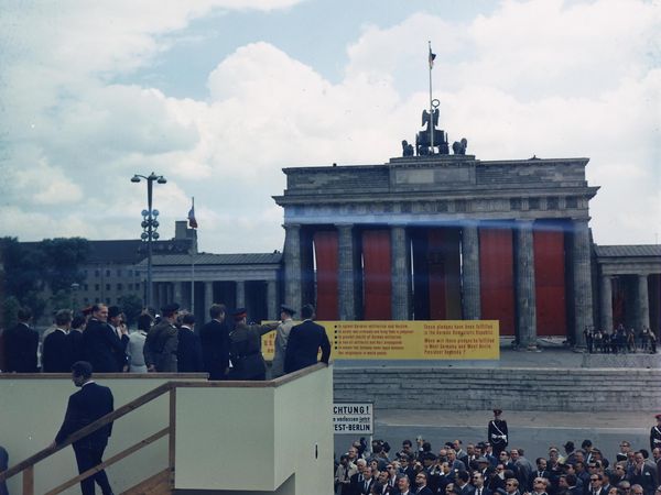 US-Präsident John F. Kennedy steht auf einem Podest und blickt auf das mit roten Tüchern verhängte Brandenburger Tor.