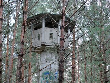Das Bild zeigt einen mit Graffiti bemalten alten Wachturm im Wald.