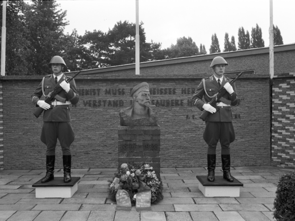 Schwarzweiß Aufnahme der Ehrenwache 1987 am Dzierzynski-Denkmal in der Kaserne des Wachregiments in Adlershof; links und rechts vom Denkmal steht ein Soldat mit Gewehr; vor dem Denkmal liegt ein Blumenkranz.