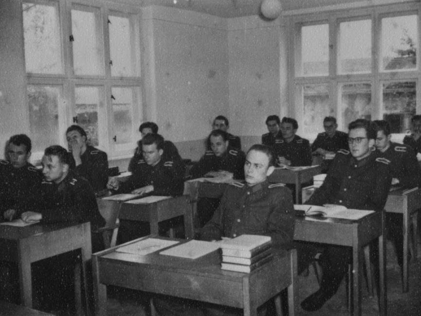 Junge Stasi-Offiziere sitzen in einem Klassenraum an Pulten.