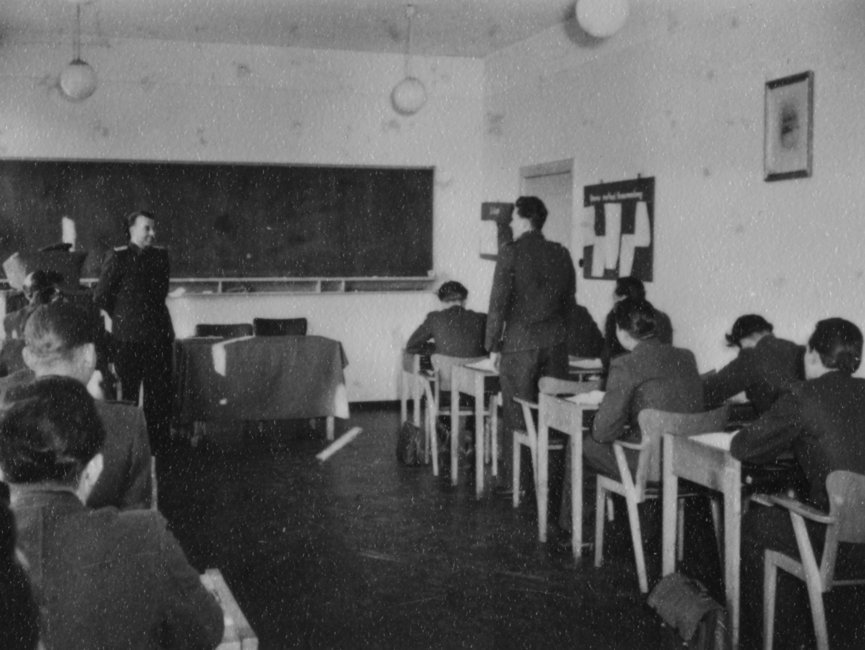 Studenten der JHS an Pulten in einem Seminarraum. Einer der Studenten steht vor seinem Pult.
