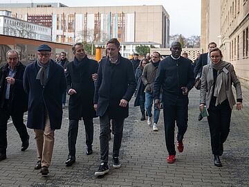 Mitglieder des Kulturausschusses des Abgeordnetenhauses Berlin laufen nebeneinander über den Campus für Demokratie.