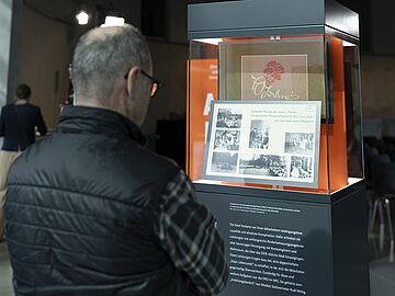 Ein Mann steht vor einer Objektstele mit einer Glasvitrine, in der sich Stasi-Fotos befinden.