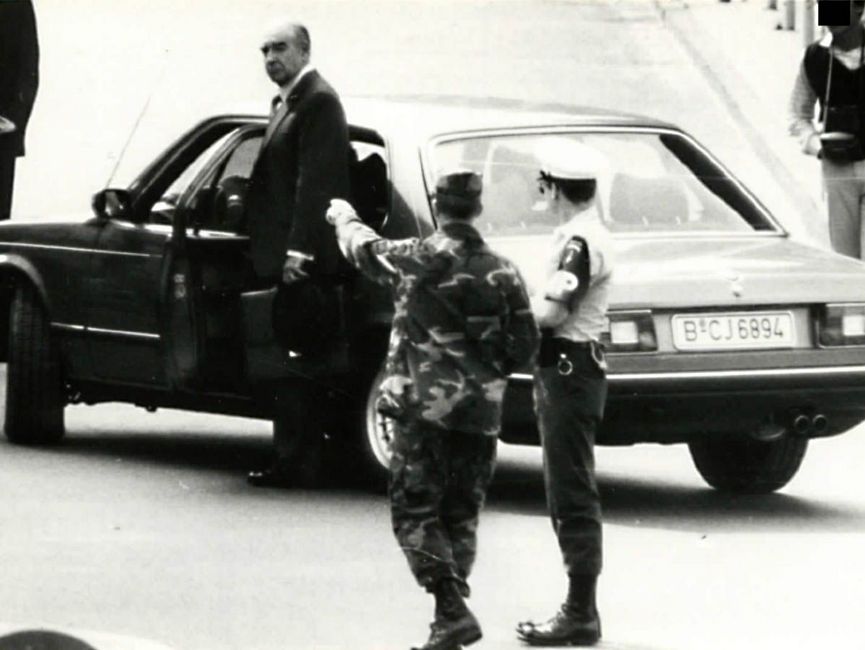 Schauspieler Robert Brown steigt aus einem BMW bei den "James-Bond-Dreharbeiten" am Checkpoint Charlie, davor stehen zwei weitere Personen in Militär- bzw. Polizeiuniform