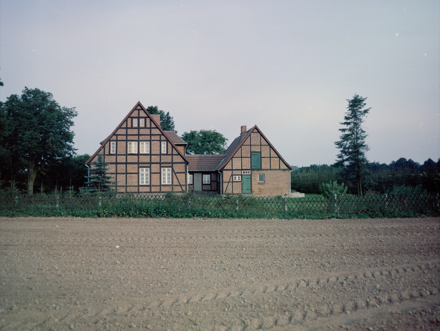 [Frontal auf die Stirnseiten zweier Häuser gerichtetes Farbfoto, das von einem Feld aus aufgenommen wurde. Die beiden Häuser sind  fest miteinander verbunden.]