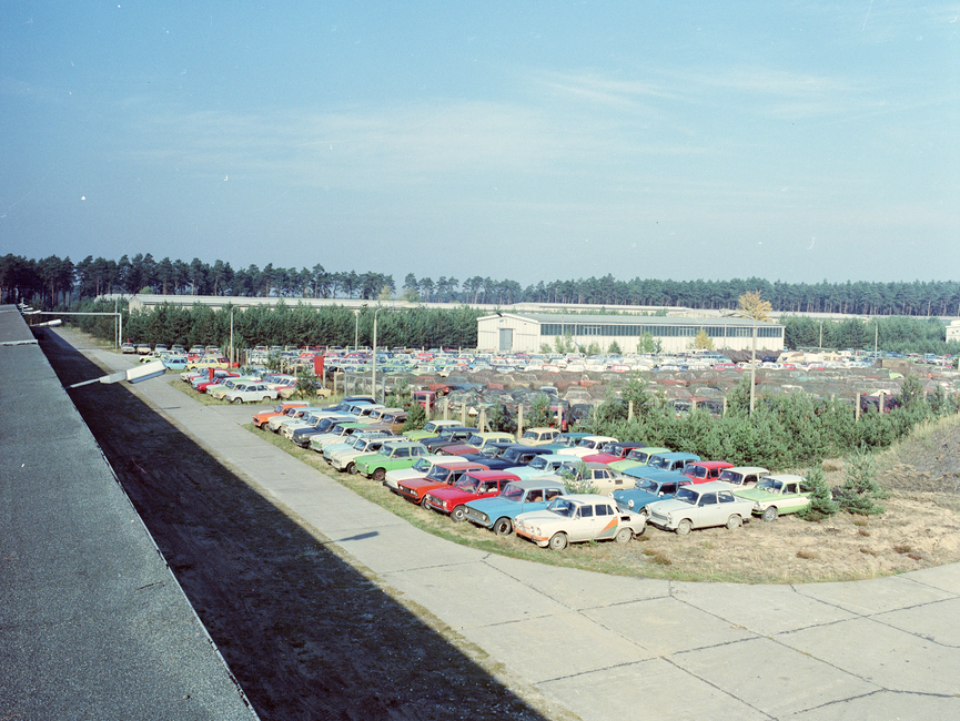 Das Bild, das vom Dach einer Lagerhalle aus fotografiert wurde, zeigt Autos in mehreren Reihen. Dahinter befindet sich eine weitere Lagerhalle.