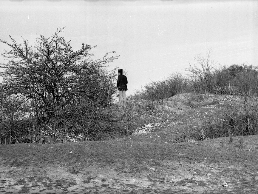Zu sehen ist ein begrünter Hügel, auf dem sich neben einem Baum ein Mann befindet, der mit dem Rücken zum Fotografen steht und sich umschaut.