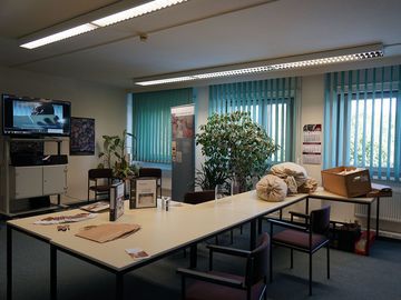 Tisch mit Informationsmaterialien des Stasi-Unterlagen-Archivs zum Thema Aktenrekonstruktion. Im Hintergrund läuft auf einem Fernseher ein Film über die Rekonstruktion von Akten.