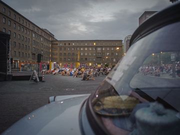 Im Vordergrund ein historischer Trabbi und ein Blick auf das Open-Air-Kino auf dem Geländer der ehemaligen Stasi-Zentrale.