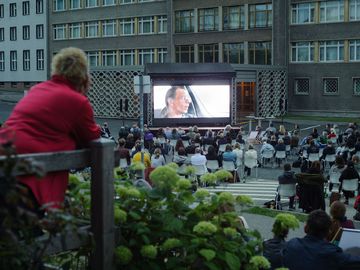 Eine große Menge Zuschauer betrachtet den im Hintergrund befindlichen Screen, auf dem der Film "Gundermann" läuft.