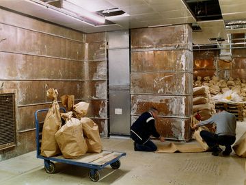 Das Bild zeigt einen mit Kupferplatten verkleideten Raum. Zwei Männer entfernen gerade eine der Platten von einer Wand.