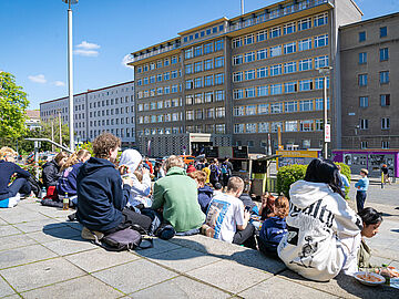 Schülerinnen und Schüler sitzen im Innenhof der ehemaligen Stasi-Zentrale mit Blick auf "Haus 1".