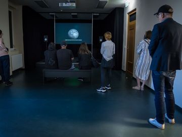 Besucherinnen und Besucher stehen vor einer Videoinstallation der 12. Berlin Biennale