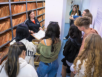 Eine Mitarbeiterin des Stasi-Unterlagen-Archivs zeigt Schülerinnen und Schülern eine MfS-Akte im Magazinraum des Stasi-Unterlagen-Archivs.