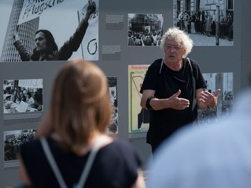 Führung auf dem Gelände der ehemaligen Stasi-Zentrale mit Tafel der Ausstellung "Revolution und Mauerfall" im Hintergrund.