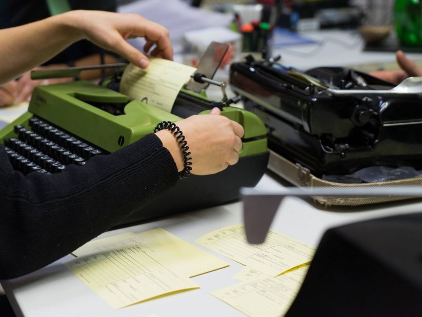 Das Bild zeigt eine grüne Schreibmaschine, in die gerade eine Karteikarte eingespannt wird.